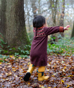 A child playing in woodland and wearing the dark maroon Little Green Radicals collecting flowers knitted collar dress.
