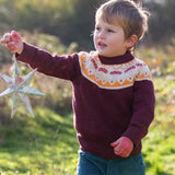 Little Green Radicals Knitted Organic Cotton Jumper in burgundy with Mushroom Fair Isle design worn by child in the forest.