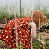 Little Green Radicals red spring birds print collared pinafore dress on a child gardening.