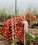 Little Green Radicals red spring birds print collared pinafore dress on a child gardening.