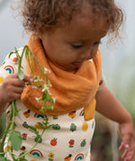 Close up of the top from the Little Green Radicals vintage style rainbows organic cotton t-shirt & jogger playset being worn with a yellow bandana style bib. A repeat pattern top featuring nature themed illustrations with cream rainbow striped trousers.