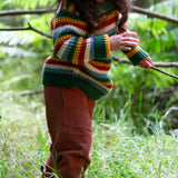 A close up of a child walking through woodland and wearing the Little Green Radicals rainbow waffle snuggly knitted jumper showing the waffle knit detail
