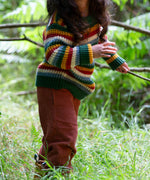 A close up of a child walking through woodland and wearing the Little Green Radicals rainbow waffle snuggly knitted jumper showing the waffle knit detail