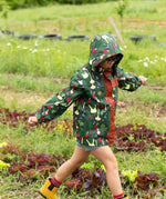 Child wearing the Little Green Radicals feast waterproof recycled kids raincoat with blue pinstripe shorts underneath with yellow wellington boots. 