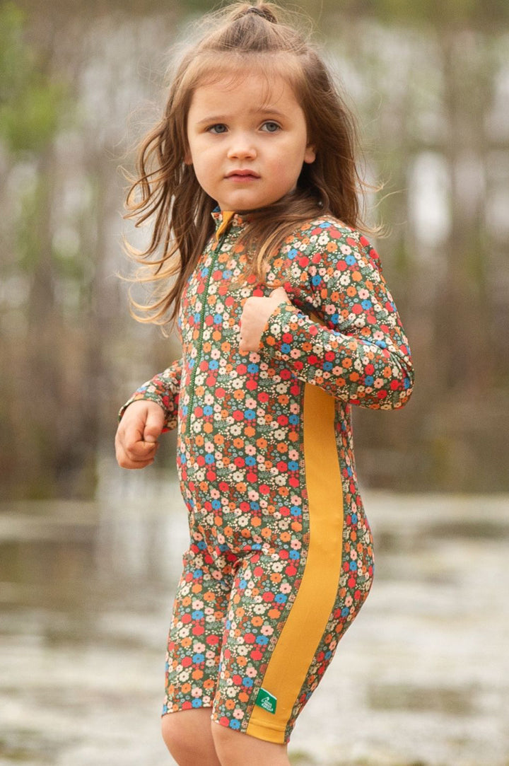child with long hair on the beach wearing the SPF fair trade swim suit by Little Green Radicals. To represent the Spring 2025 SALE at Babipur on LGR brand.