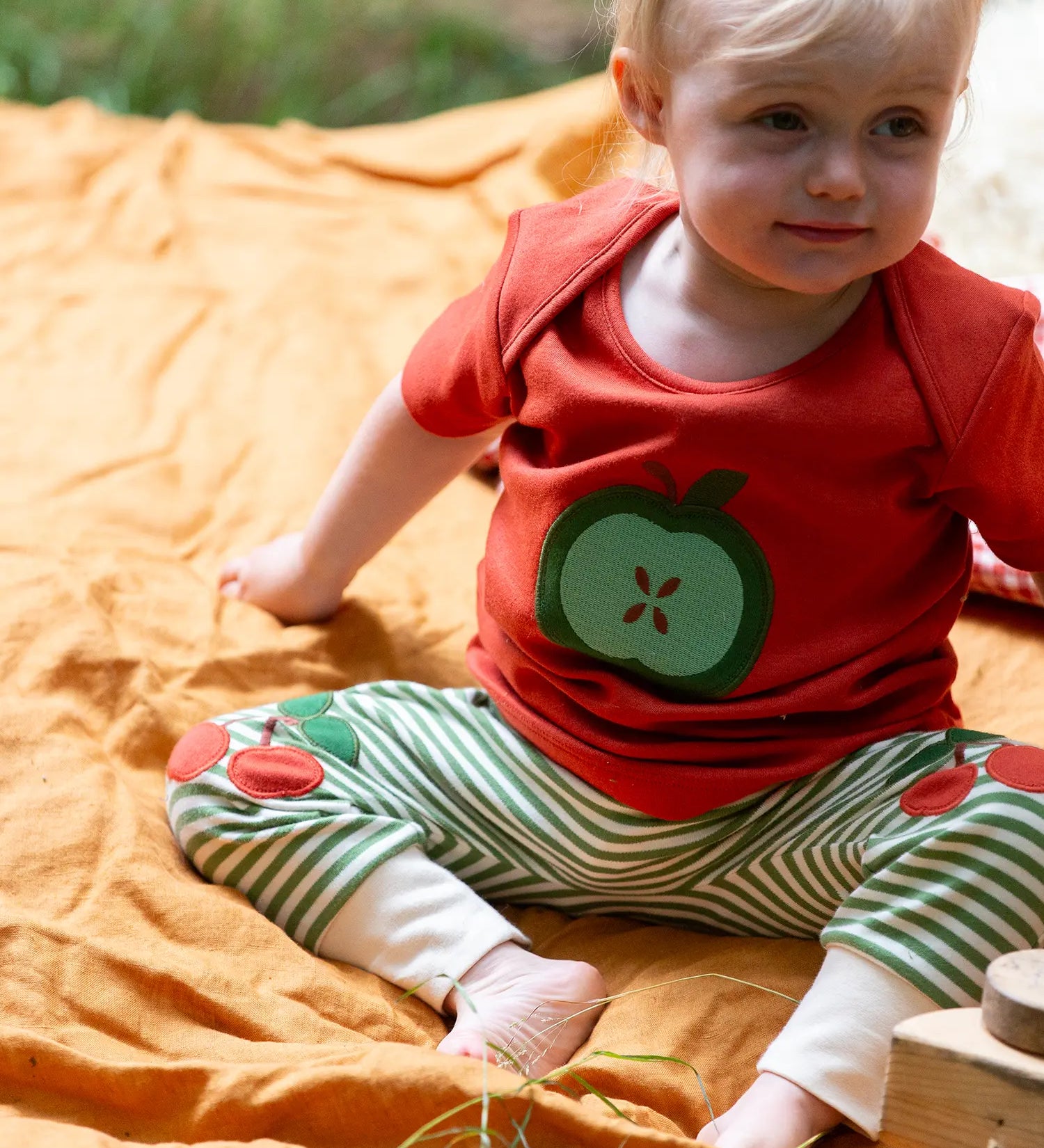 Child wearing the Little Green Radicals green apple applique organic short sleeve red t-shirt with cherry knee patch joggers.