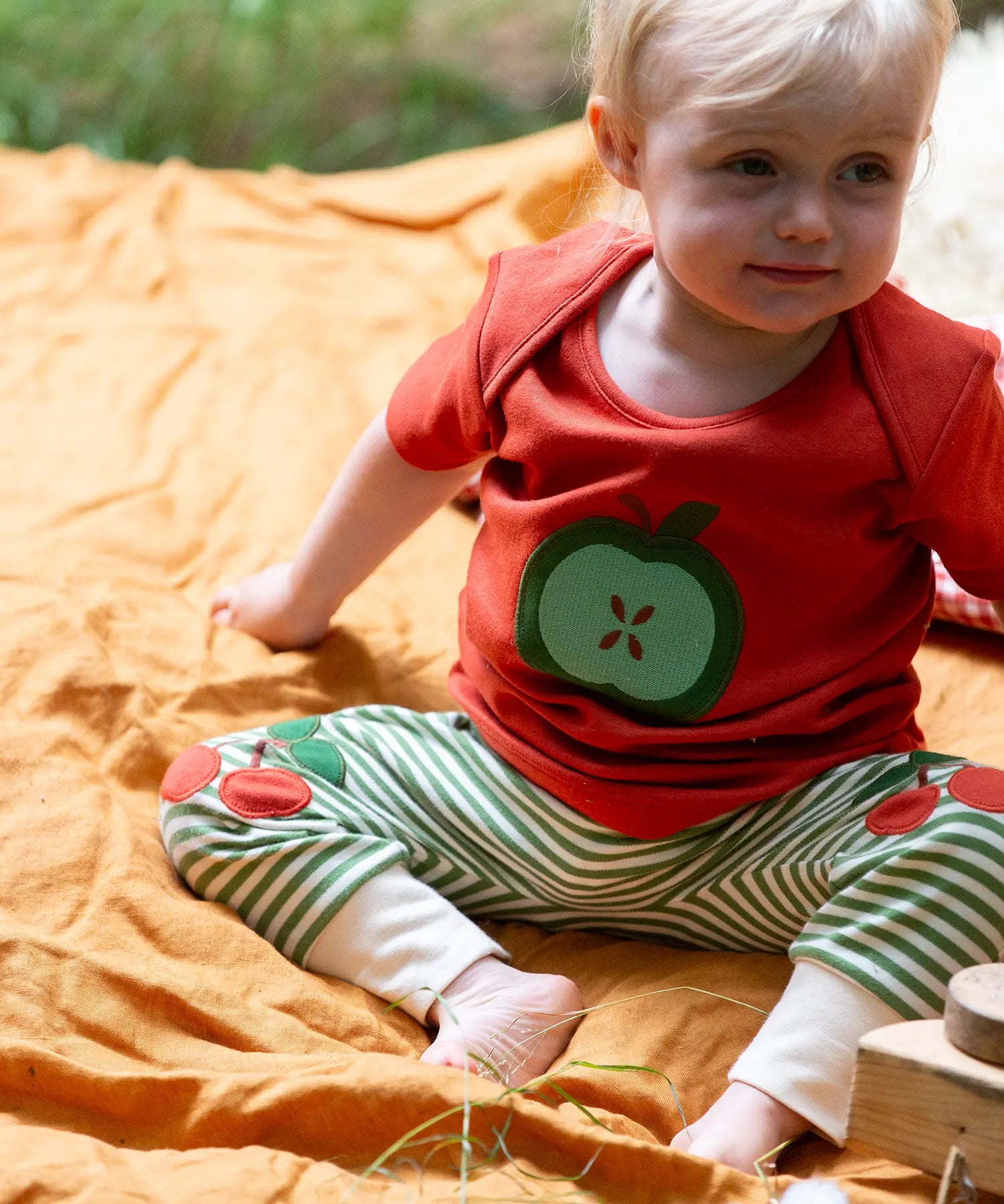 Child wearing the Little Green Radicals green apple applique organic short sleeve red t-shirt with cherry knee patch joggers.