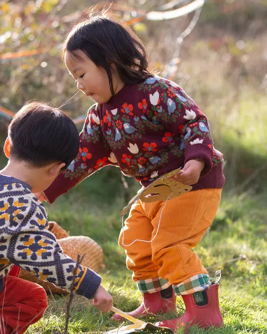 Little Green Radicals knitted jumper in plum with bird design, made from organic and Fairtrade certified cotton, worn by a child in yellow trousers.