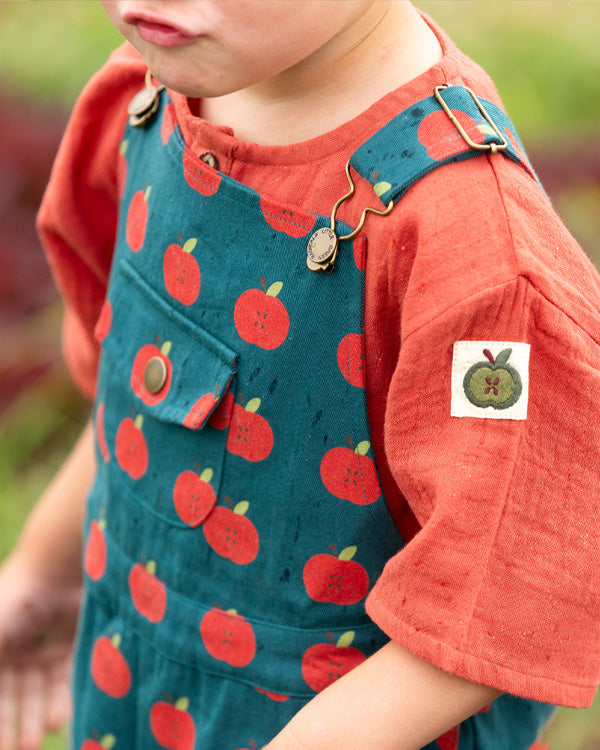 Close up of apple Dungarees in blue by Little Green Radicals, paired with a red muslin top to represent Little Green Radicals at Babipur. 