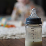 A Lola & Lykke bottle, with the Nipple Teat attached. A baby is in the background but is blurred as the image focuses on the bottle