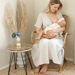 An adult breastfeeding a baby, with the Lola&Lykke Smart Electric Breast Pump on a table next to them.
