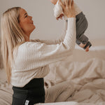 A person holding a baby in the air, wearing the Lola & Lykke Core Restore Postpartum Belly Band