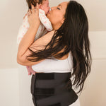 A person holding a baby, wearing the Lola & Lykke Core Restore Postpartum Belly Band