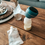The Lola&Lykke Smart Electric Breast Pump and milk bag next to the pump. Both items are set on a wooden table