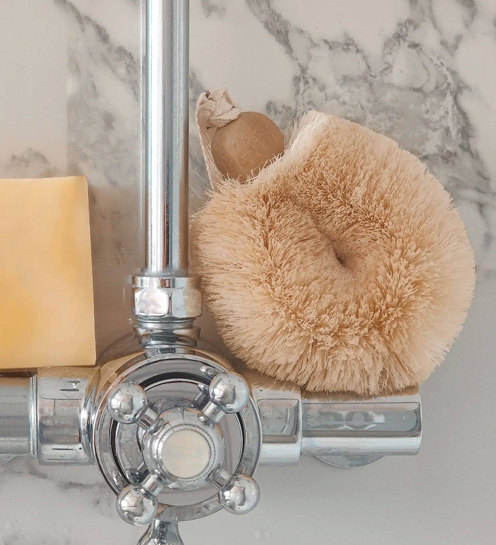 LoofCo sisal shower puff brush resting on a shower tap next to a soap bar