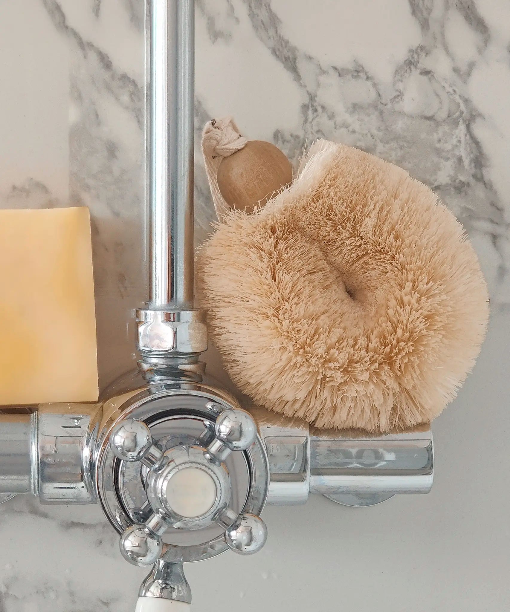 LoofCo sisal shower puff brush resting on a shower tap next to a soap bar