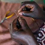 A look at the intricate hand making process. A person carefully threads gold and black glass beads onto copper wire