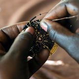 A look at the intricate hand making process. A person carefully threads gold and black glass beads onto copper wire
