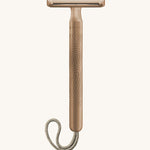 A rose gold Muhle steel safety razor with a natural cord on a cream background
