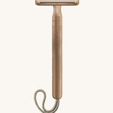 A rose gold Muhle steel safety razor with a natural cord on a cream background