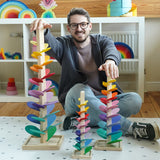 Comparison of Magic Wood Marble trees: mini, small and large next to a man in the Babipur playroom. Satisfying wooden marble runs made of a tall stem, rainbow leaves and marbles.