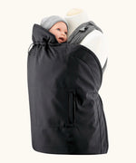Mamalila black universal softshell babywearing cover over a carrier with a baby doll. Showing hood behind the head and side pockets.