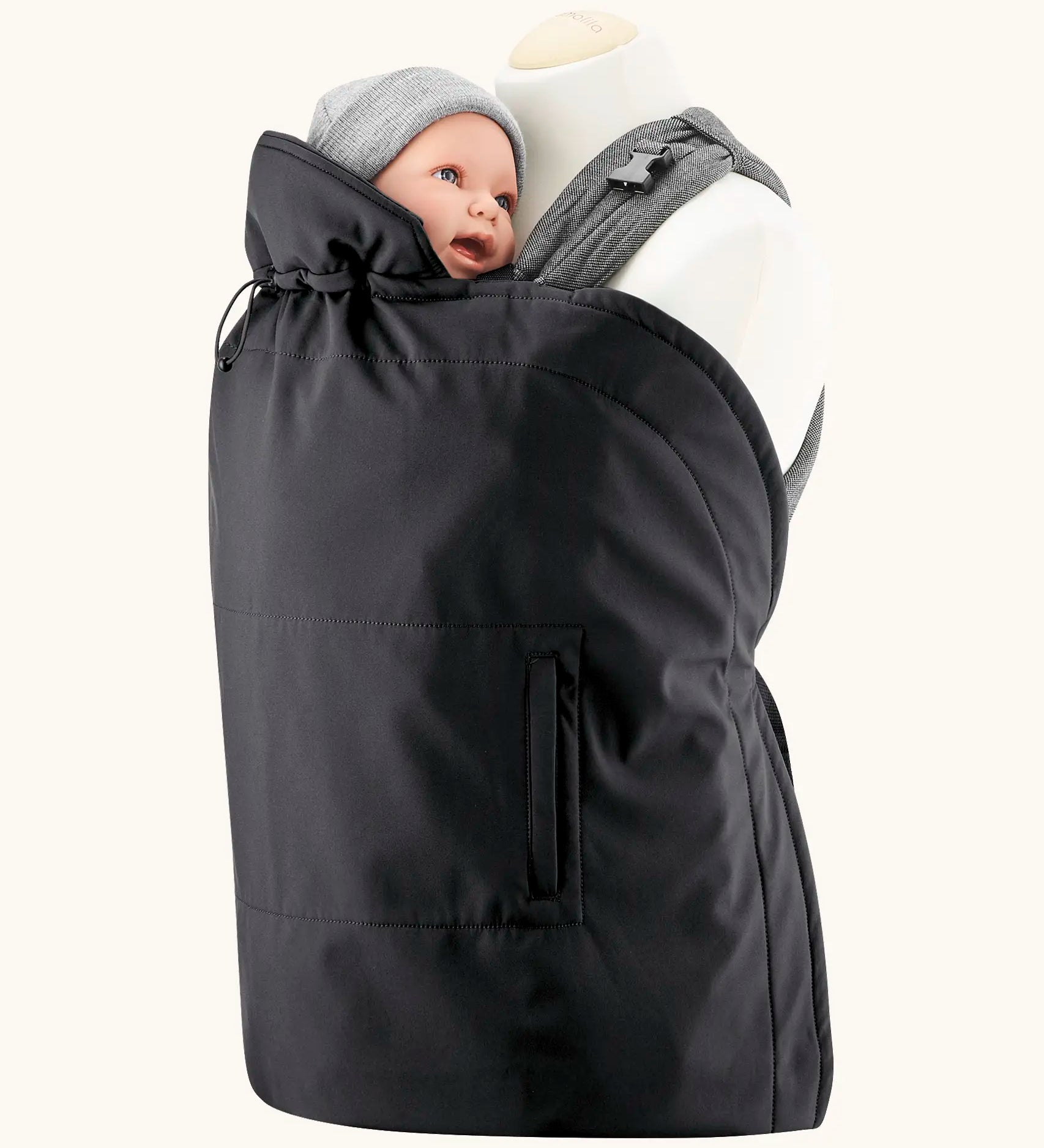 Mamalila black universal softshell babywearing cover over a carrier with a baby doll. Showing hood behind the head and side pockets.