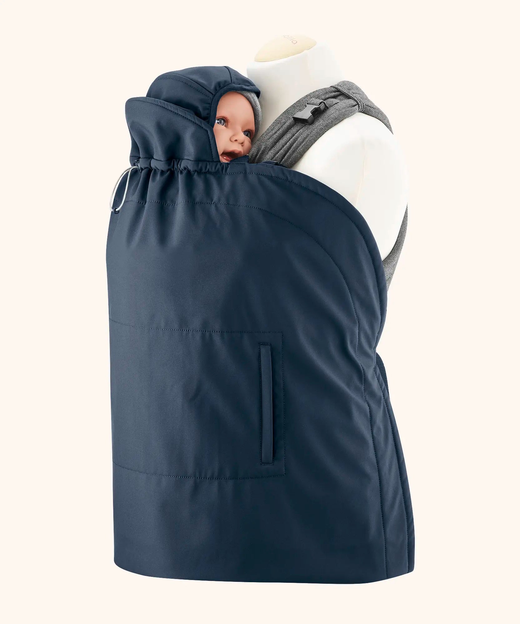 Mamalila navy universal softshell babywearing cover over a carrier with a baby doll. Showing protective hood over the head and side pockets.