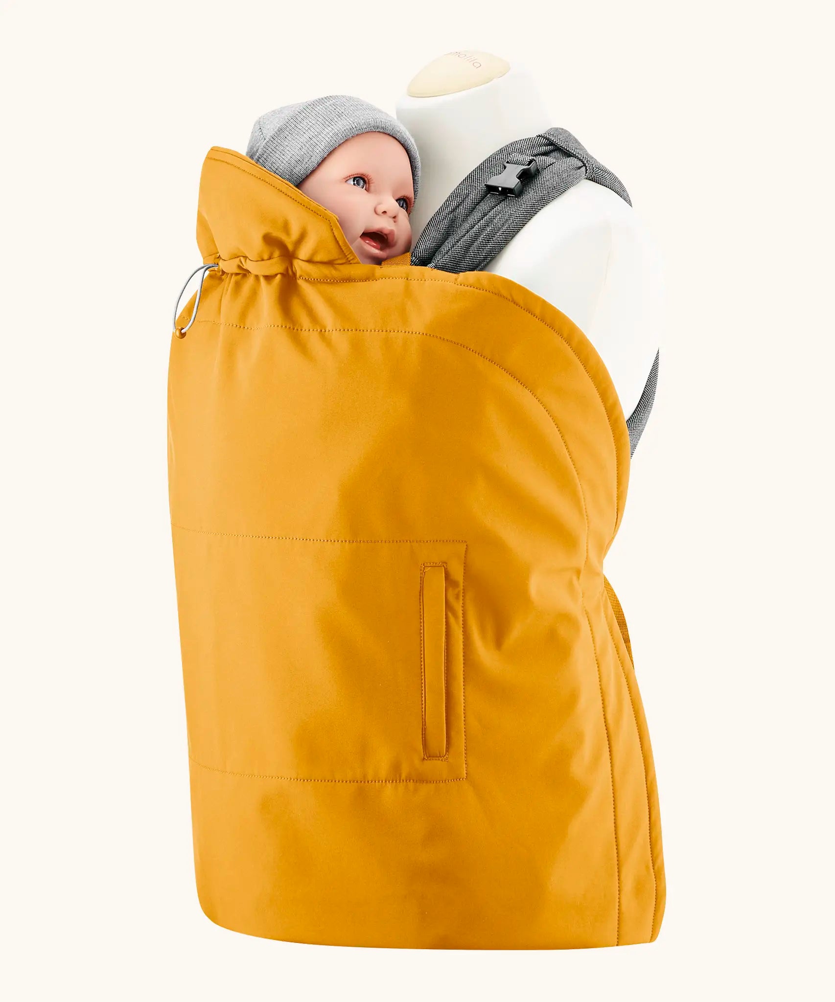 Mamalila yellow universal softshell babywearing cover over a carrier with a baby doll. Showing hood behind the head and side pockets.