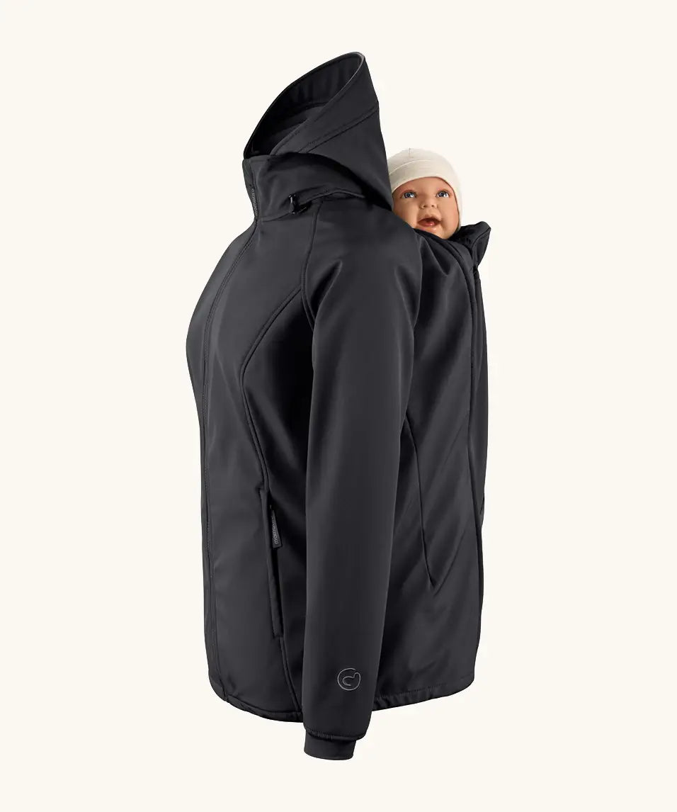 Mamalila soft shell baby wearing allrounder fitted jacket in black showing a baby doll sitting on the back with the protective hood down