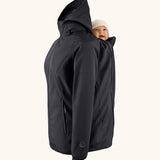 Mamalila soft shell baby wearing allrounder fitted jacket in black showing a baby doll sitting on the back with the protective hood down