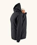 Mamalila soft shell baby wearing allrounder fitted jacket in black showing a baby doll sitting on the back with the protective hood down