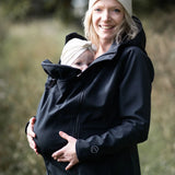 A mother wearing the Mamalila soft shell baby wearing allrounder fitted jacket in black carrying a baby on the front