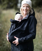A mother wearing the Mamalila soft shell baby wearing allrounder fitted jacket in black carrying a baby on the front