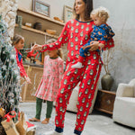 A woman wearing a Maxomorra Swedish Santa Adult Long Sleeve Pyjama Set holding a small child that is wearing a reindeer print rompersuit. 