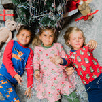 Three children lying on the floor looking up at the camera wearing clothing from the Maxomorra Christmas collection. 