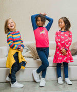 Three children wearing Maxomorra, the first is wearing stripes, the child in the middle is wearing a unicorn raglan top and the third child is wearing the Maxomorra Unicorn Long Sleeve Circle Dress.