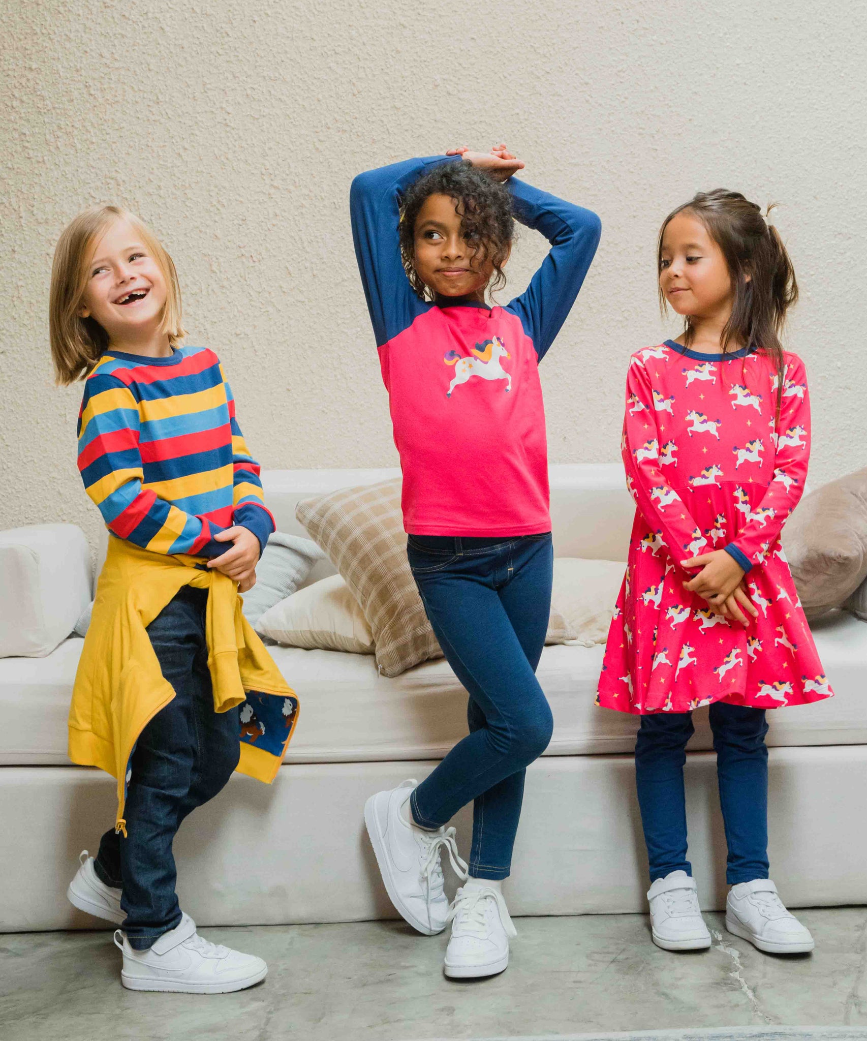Three children wearing Maxomorra, the first is wearing stripes, the child in the middle is wearing a unicorn raglan top and the third child is wearing the Maxomorra Unicorn Long Sleeve Circle Dress.