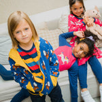 A child wearing a Maxomorra Wolf Reversible Zip Hoodie. Two other children can be seen in the background lying on a sofa.