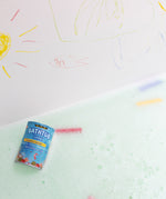 The Medenka beeswax bath crayons and their box floating in a bubbly bath tub.
