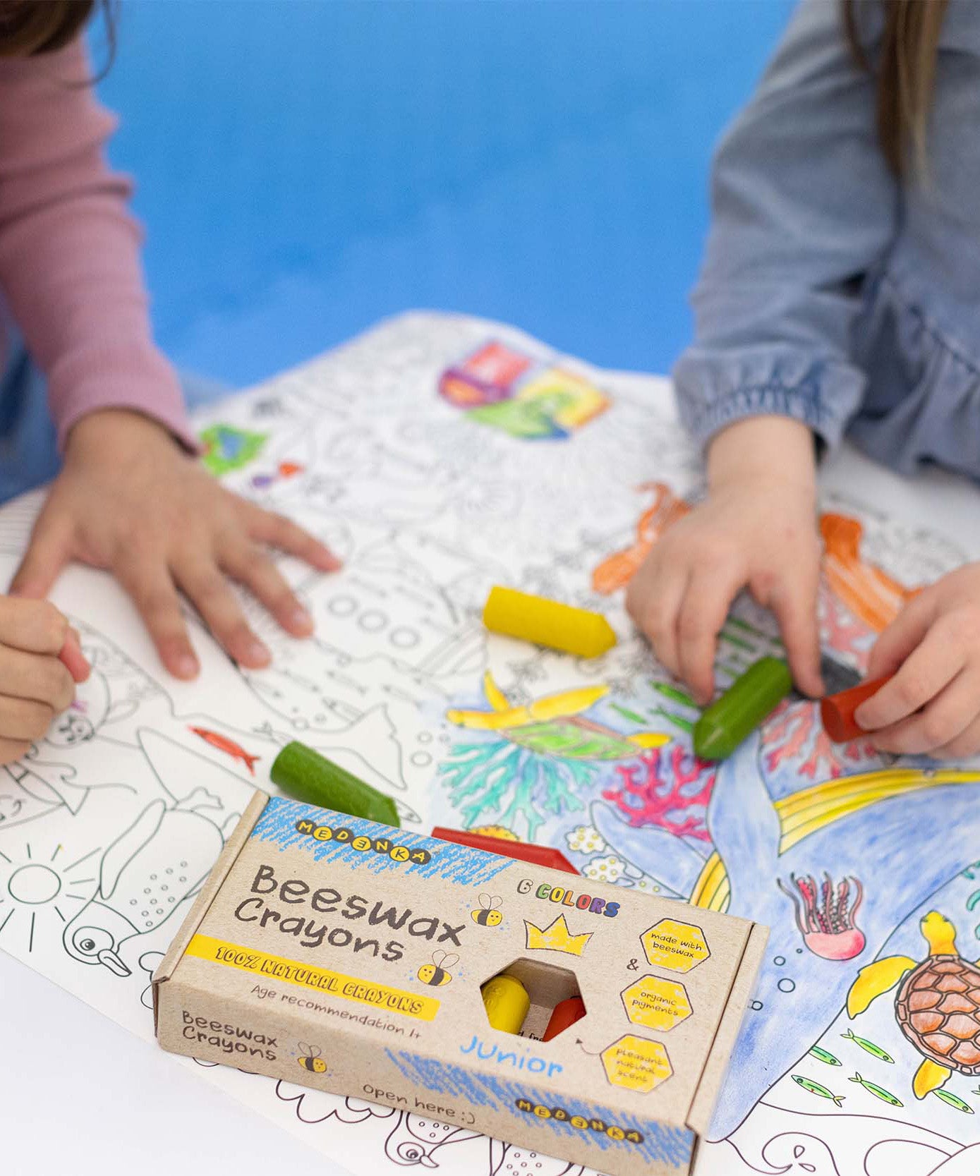 A closeup of children using the Medenka natural beeswax crayons to colour in an ocean drawing. 
