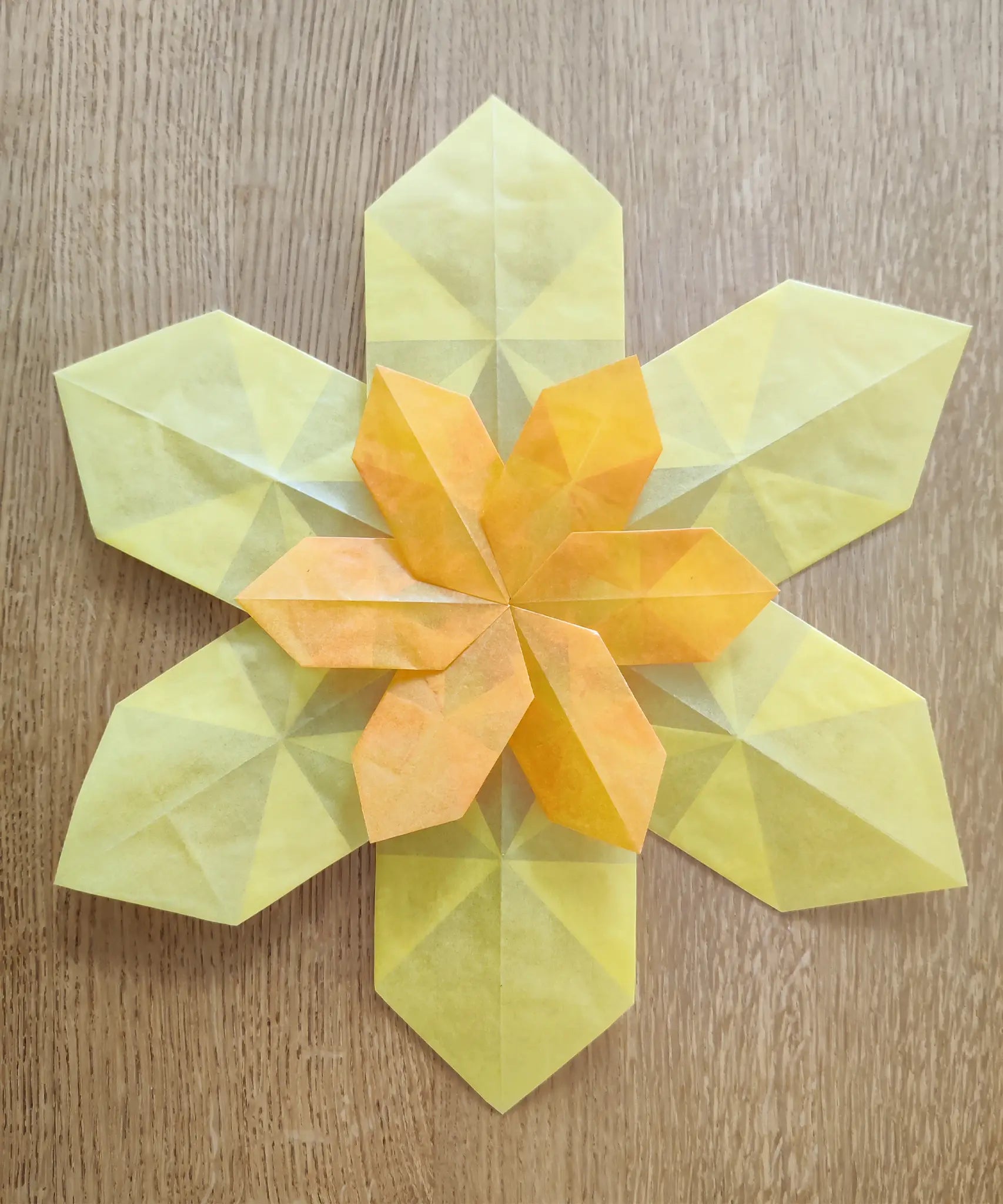 Yellow daffodil made from Kite waxed paper lying flat on a wooden surface