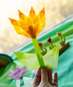 Adult hand holding a yellow flower made from Kite waxed paper