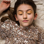A child wearing the gold makeup from the Namaki Gold Fox Sparkling Pouch, whilst lying down with their eyes closed 