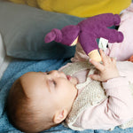 A baby playing with a purple Nanchen Waldorf Pimpel doll, looking at the face of the doll in delight