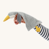 A person has the Nanchen Baby Comforter - Grey Goose resting on their arm, and underneath the head is a small hole to use the comforter as a finger puppet. The image is on a cream background