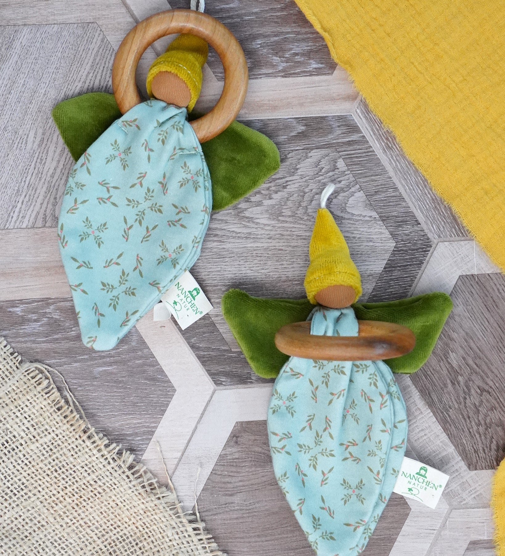 Pair of Nanchen flower fairies, an organic cotton floral grasping baby toy with a wooden ring, green velour wings and yellow pointed hat and a loop for hanging, for sale at Babipur.