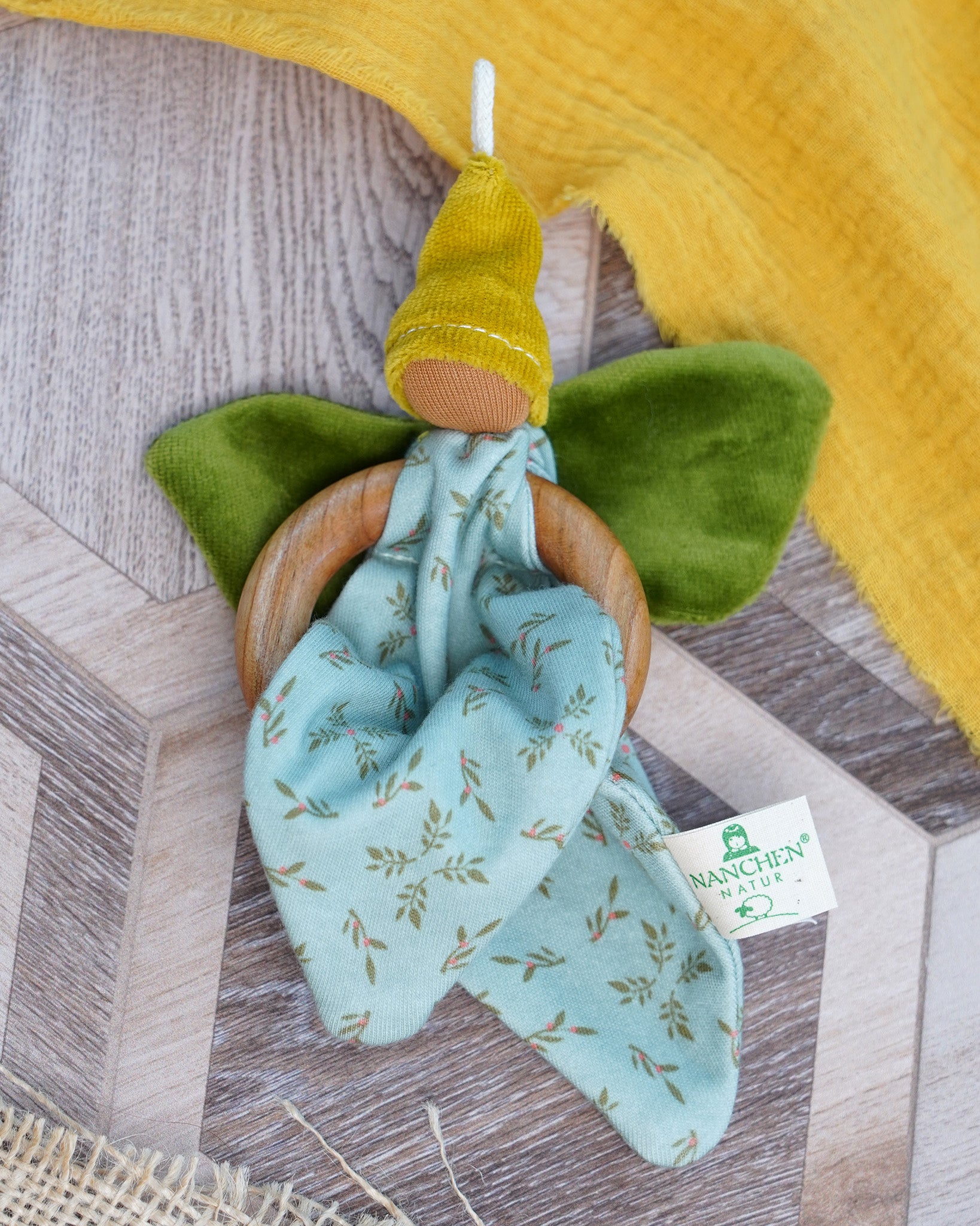 Nanchen flower fairy, crafted from organic cotton with wooden ring, green velour wings, yellow pointed hat, and hanging loop, buy now at Babipur.