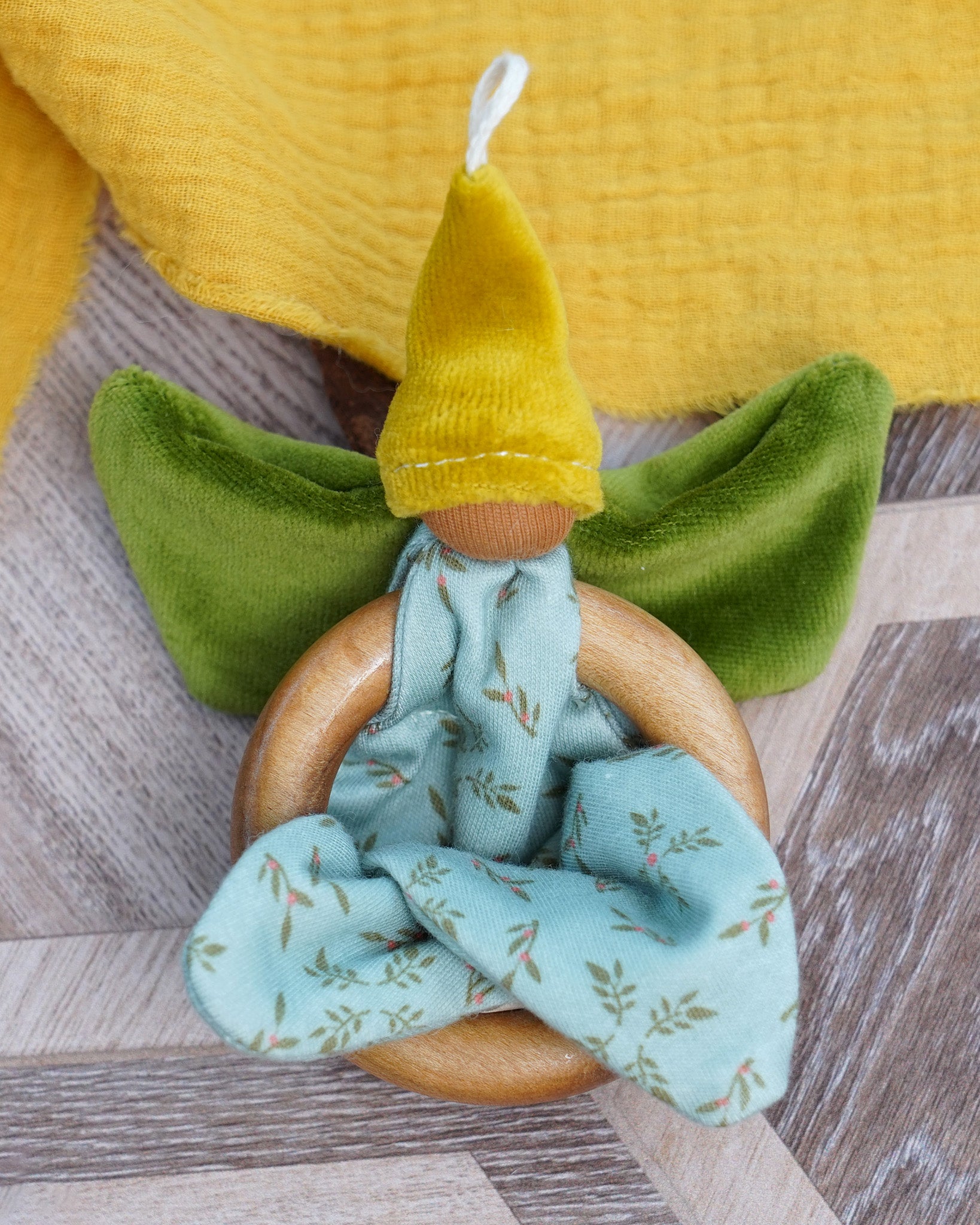 Nanchen organic cotton flower fairy baby toy featuring wooden grasping ring, soft green velour wings, yellow pointed hat, and loops for hanging, sold at Babipur.