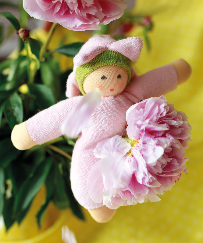 The Nanchen Flower Fairy Rattle Doll - Pink is sat on a beautiful pink rose